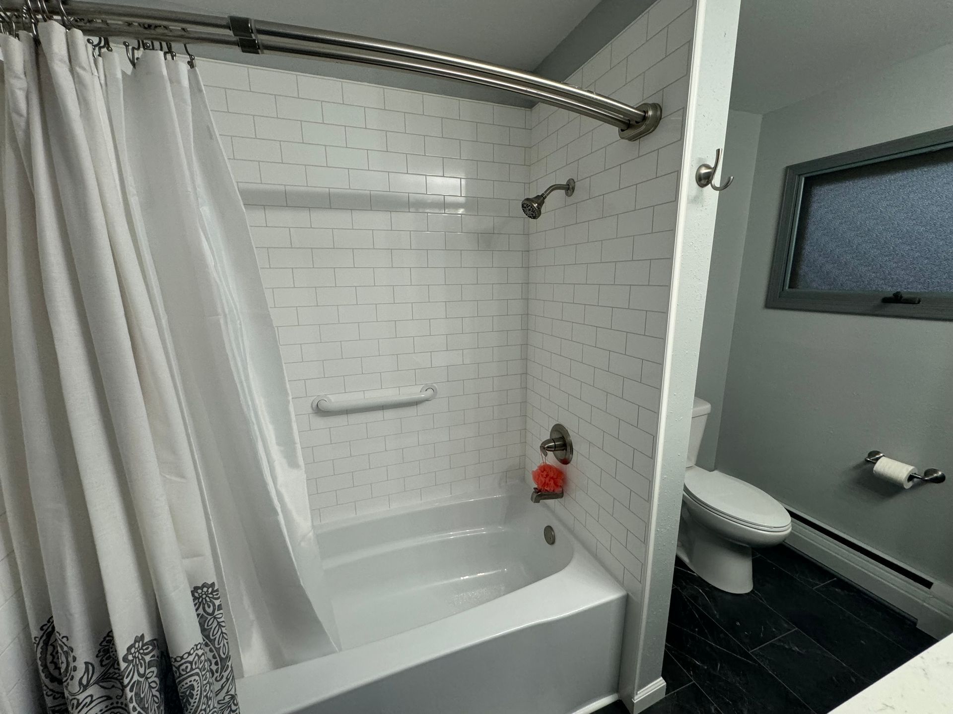 A bathroom with a tub, shower, toilet and window