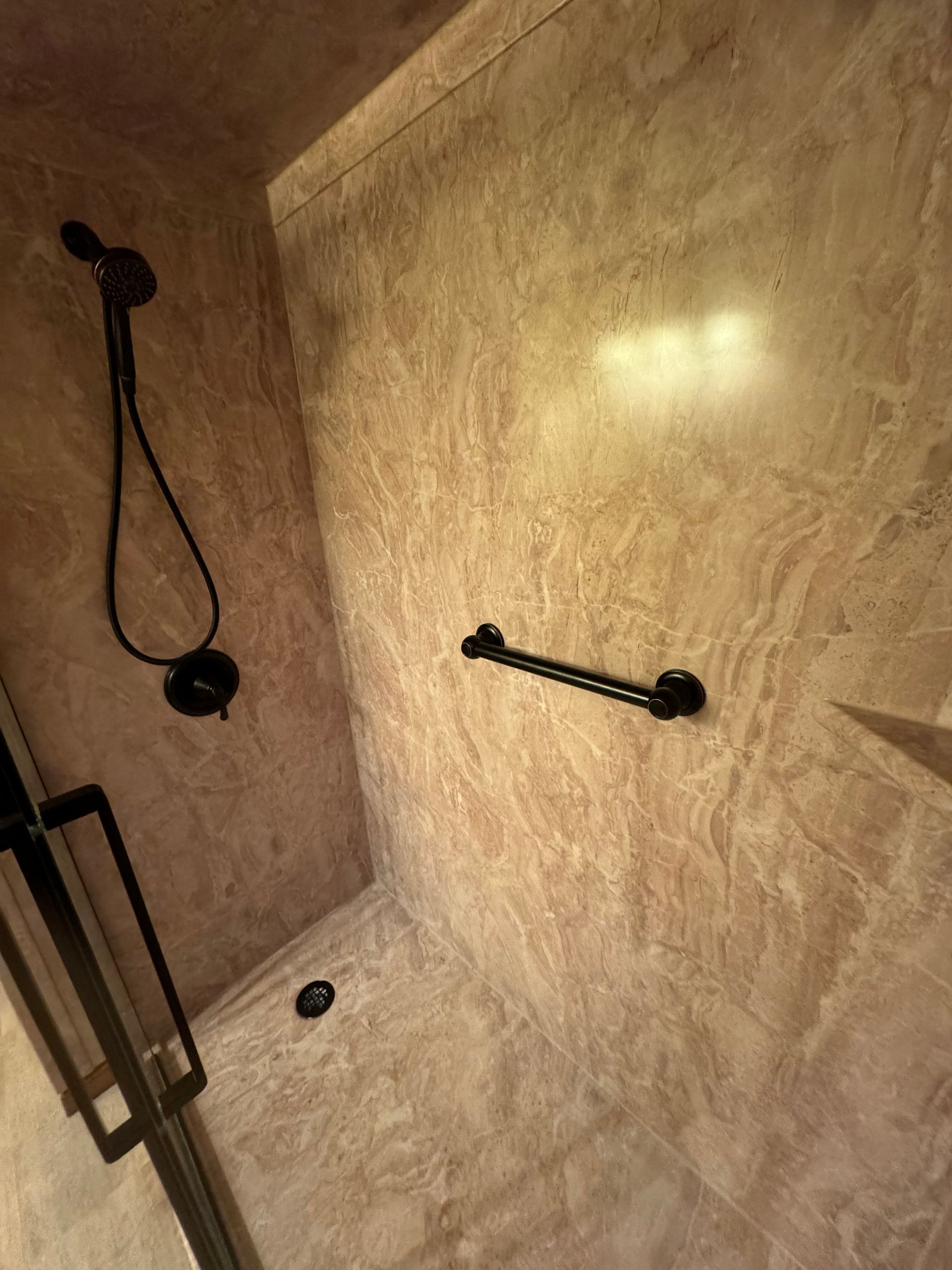 A shower stall with a hand rail and a shower head