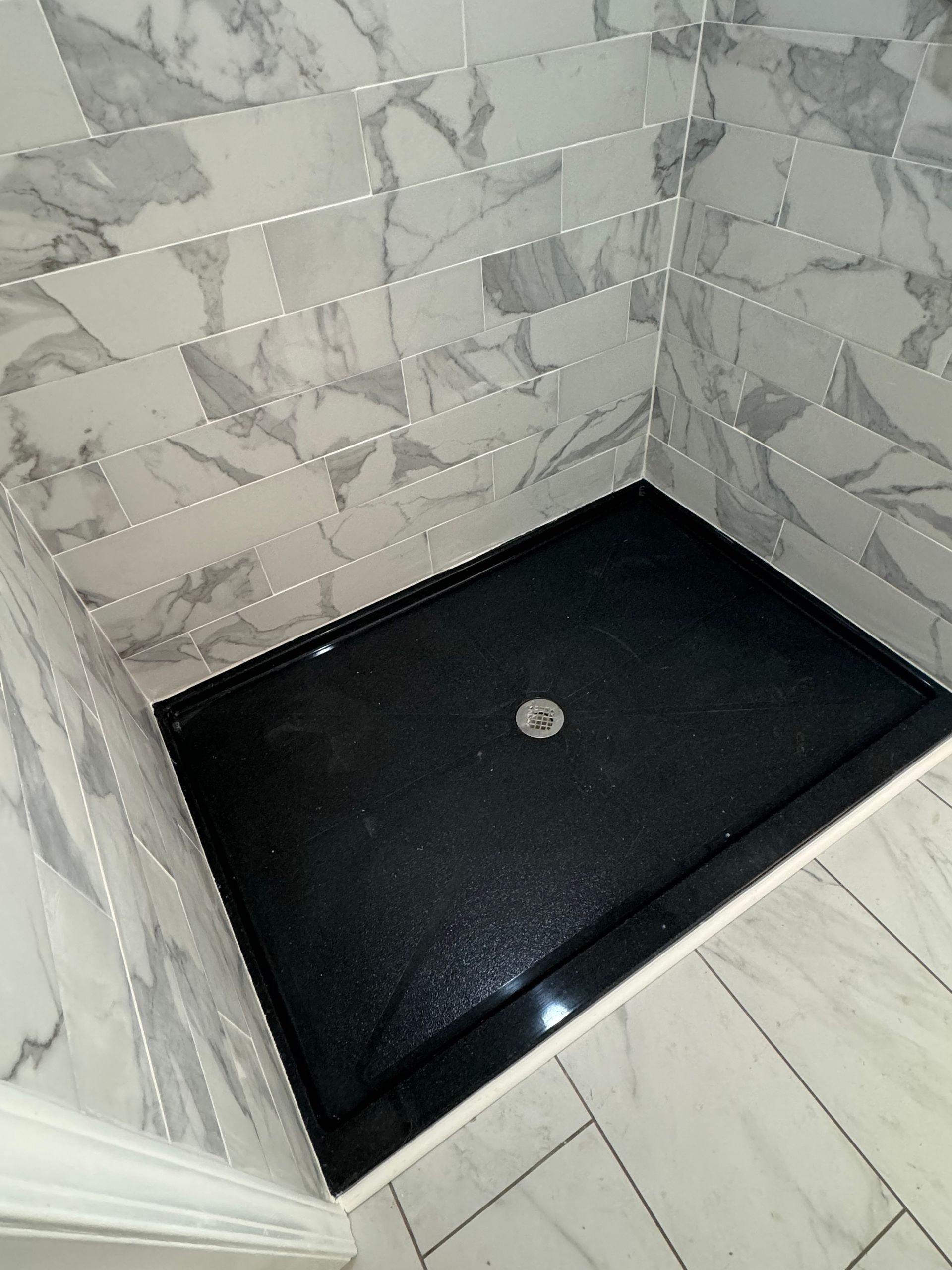 A black shower stall in a bathroom with marble tiles
