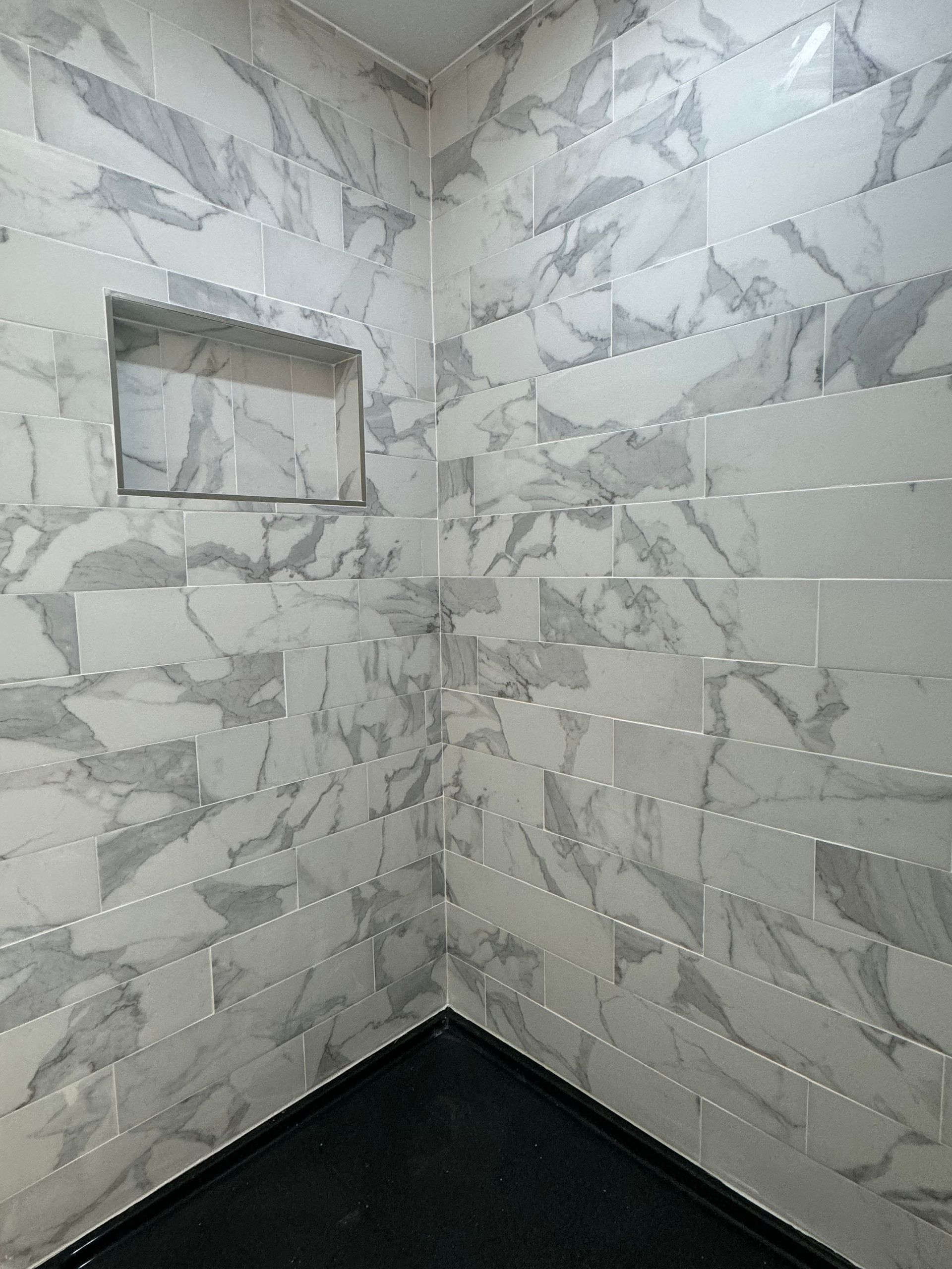 A bathroom with marble tiles on the walls and a black floor