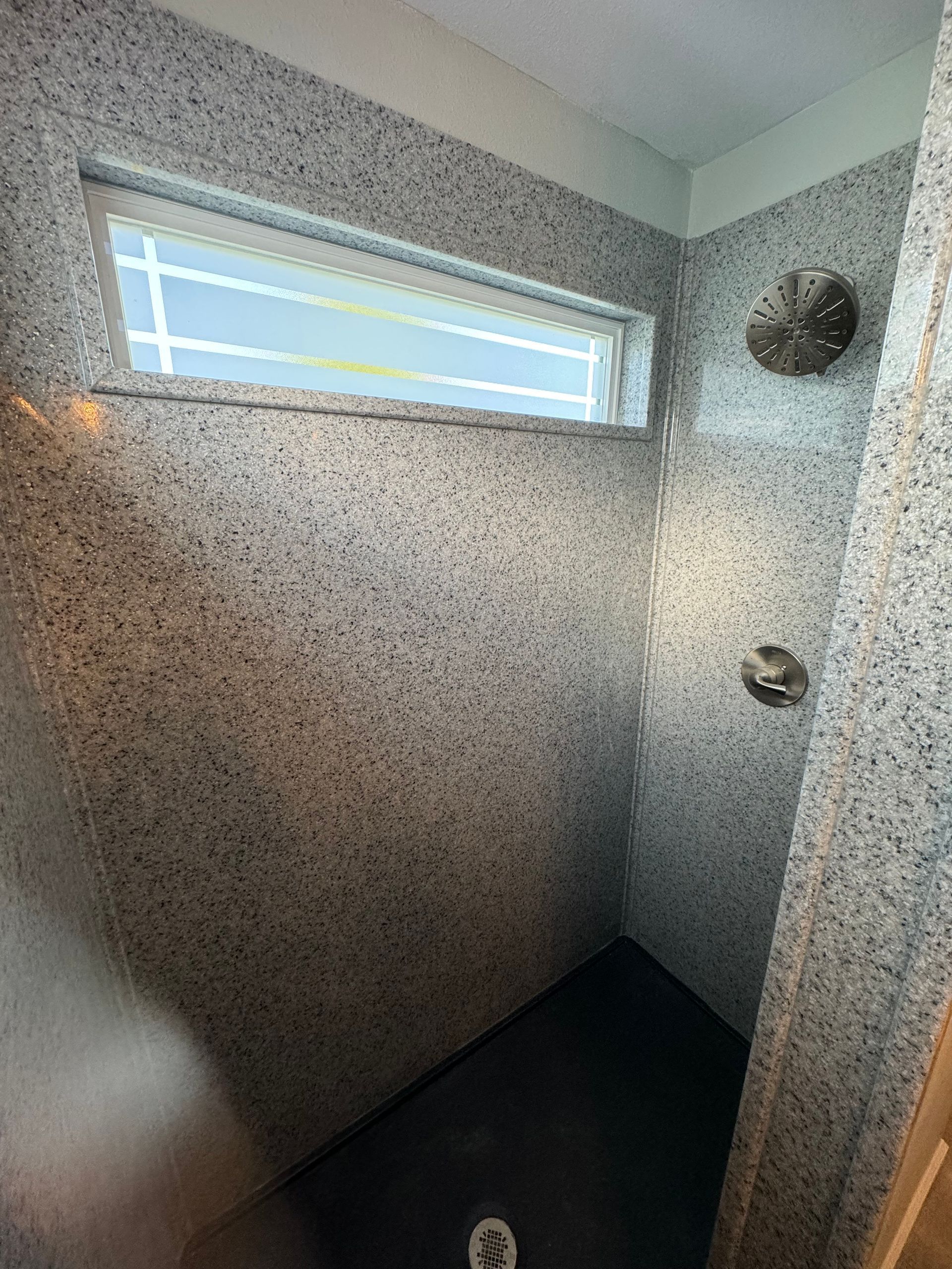 A walk-in shower with a window and a shower head