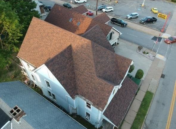 High-angle view of a light blue building with a brown roof, street, and parked cars visible.