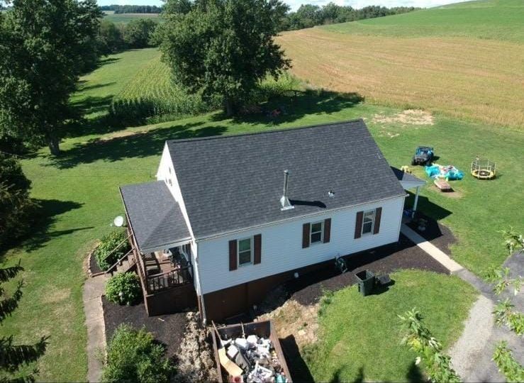 Aerial view of a white house with a dark gray roof on a green lawn in a rural setting.