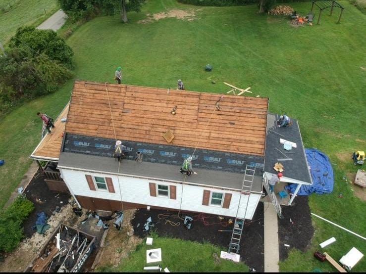 Roofers working on a house, placing shingles. Brown roof, white house with brown shutters.