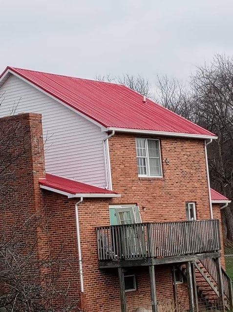 Two-story brick house with a red metal roof, white siding, a wooden deck, and a brick chimney.