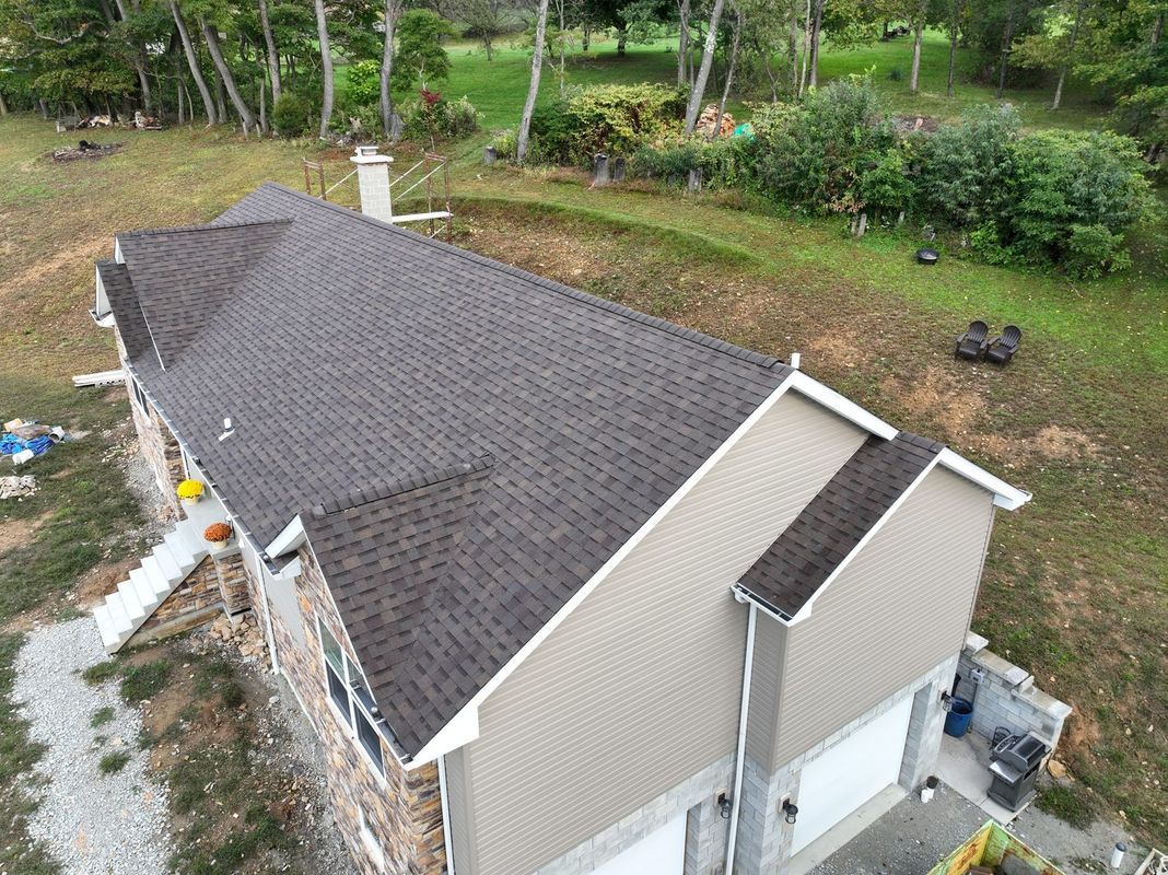 Aerial view of a house with a brown shingled roof, beige siding, and a green lawn.