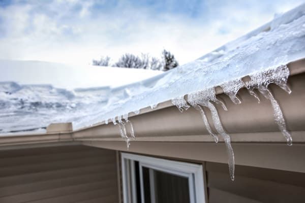 Snow and ice on a roof with icicles hanging from the gutter in winter.