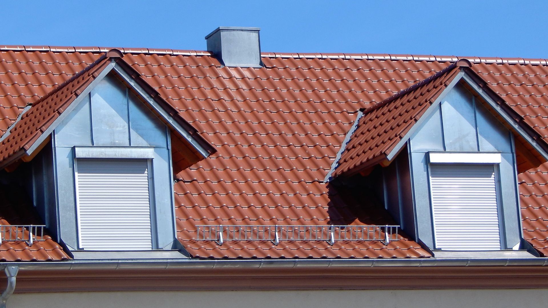 Red tiled roof with two dormers featuring metal trim and closed white shutters.