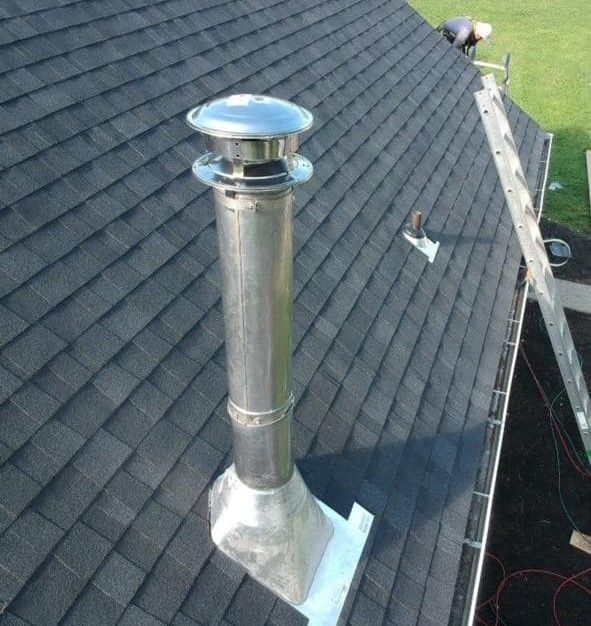 Metal chimney on a black shingle roof, person on roof, ladder visible.