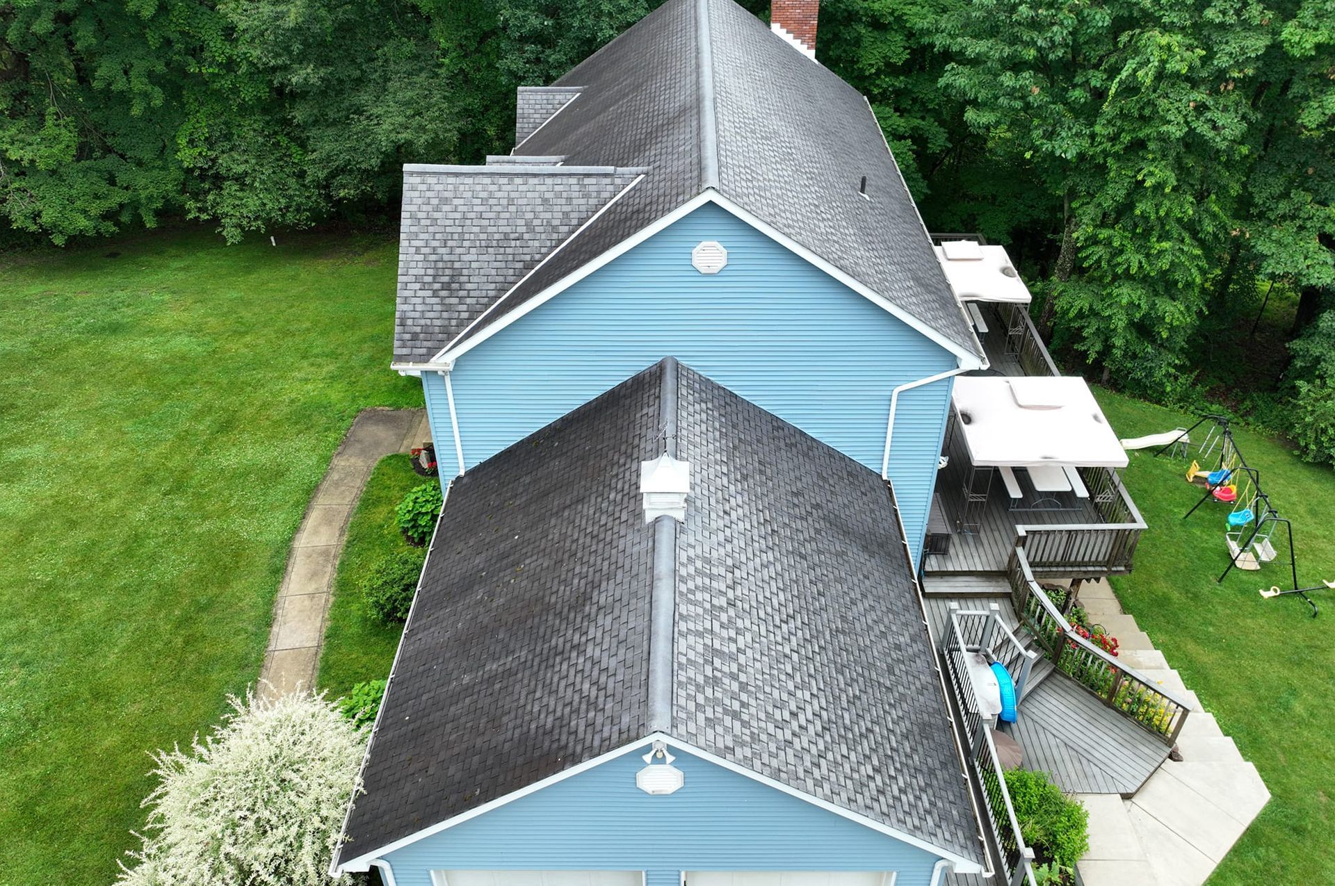 Blue house with a dark roof, surrounded by green lawn and trees.