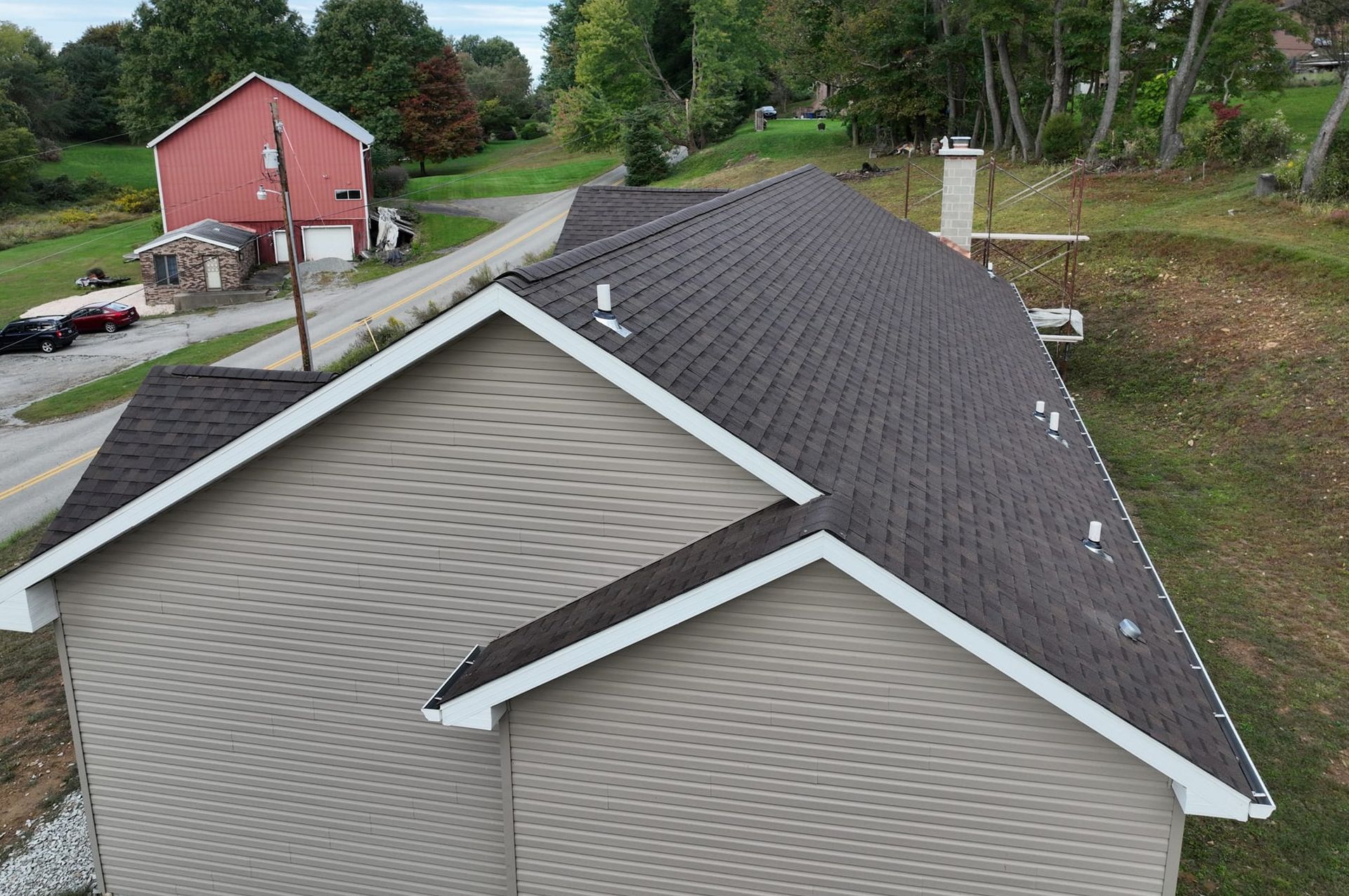 House with gray siding and brown shingle roof, white trim, chimney, rural setting.