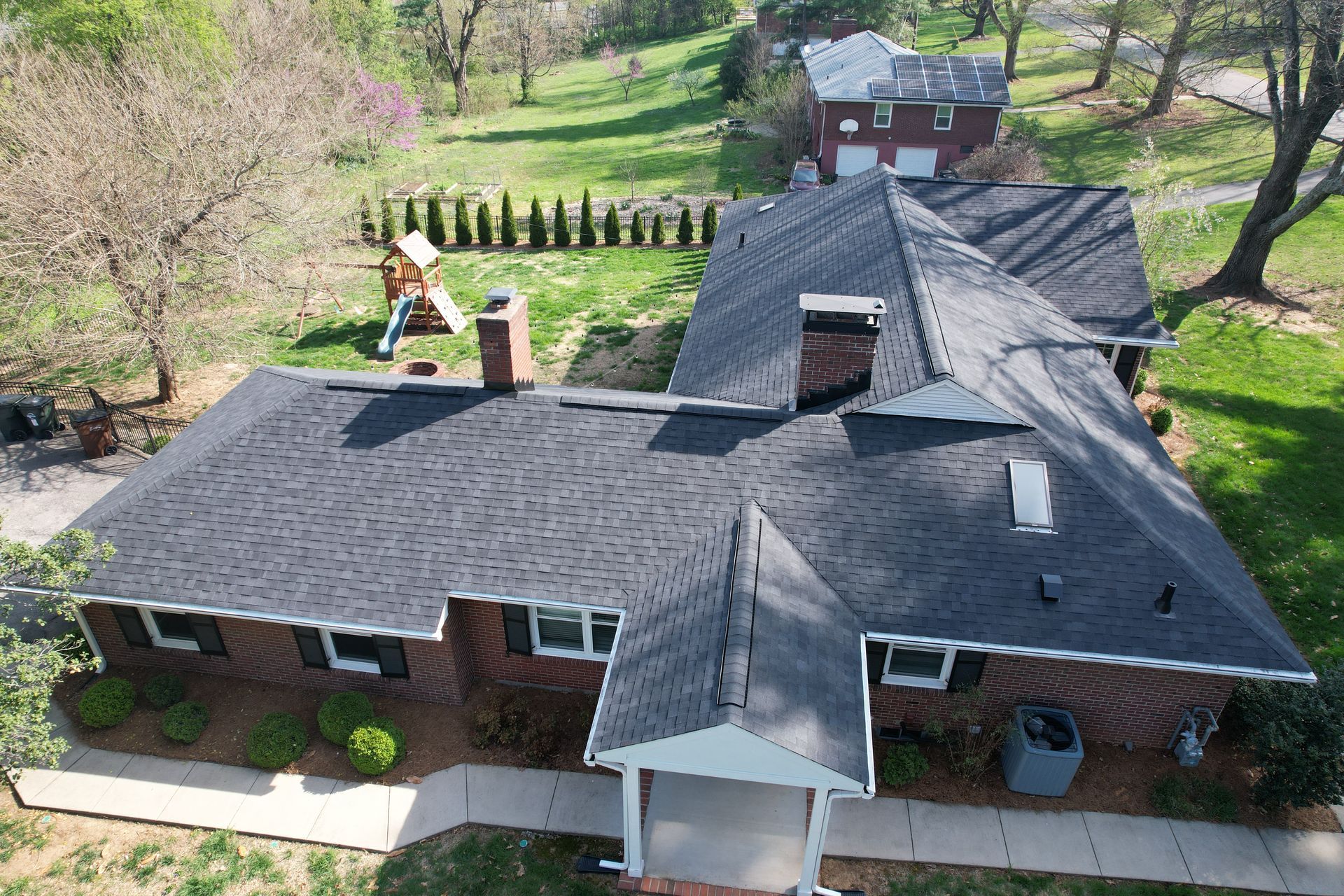 Aerial view of a brick house with a dark roof, surrounded by green trees and lawn