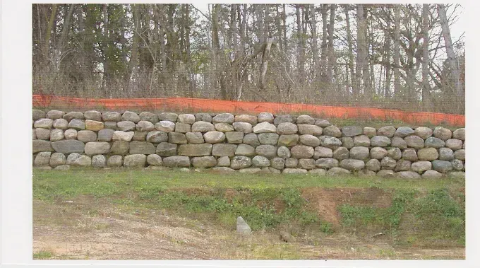 Stone retaining wall with orange safety fence in a wooded area