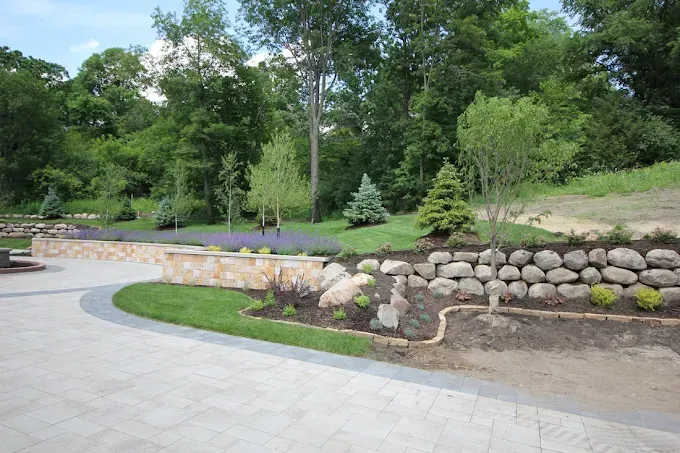 Curved stone retaining wall beside a paved path in a green landscaped park area