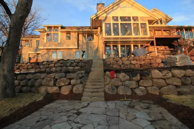 Stone staircase leading to a large tan house with a glass-walled sunroom at sunset