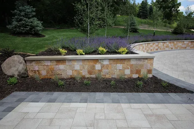 Stone retaining wall with purple flowers beside a paved patio and landscaped backyard