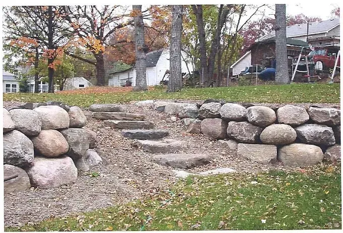 Stone steps built into a hillside in a park, bordered by large rocks and autumn trees.