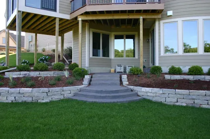 Front porch with stone steps, green lawn, and landscaped flower beds on a house exterior