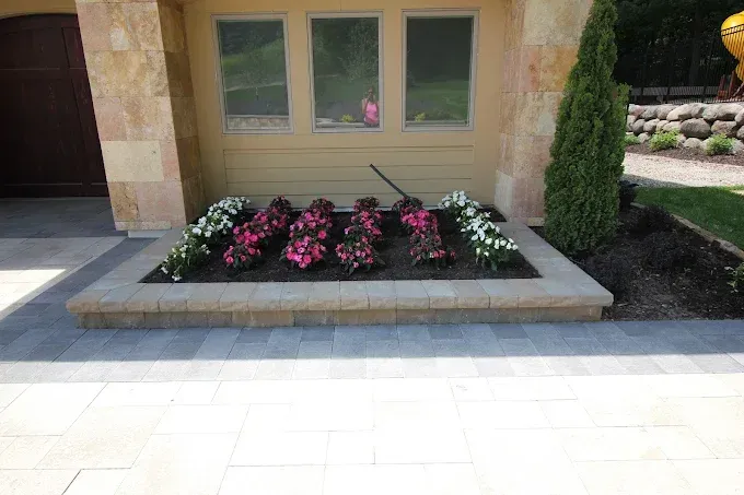 Front entrance with a raised concrete planter of pink and white flowers beneath windows.