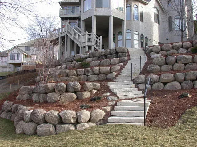 Stone retaining walls and stairs leading up to a house on a sloped yard.