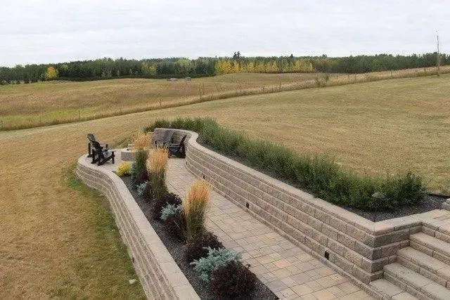 Curved brick walkway through a grassy field with benches and small shrubs, under an overcast sky
