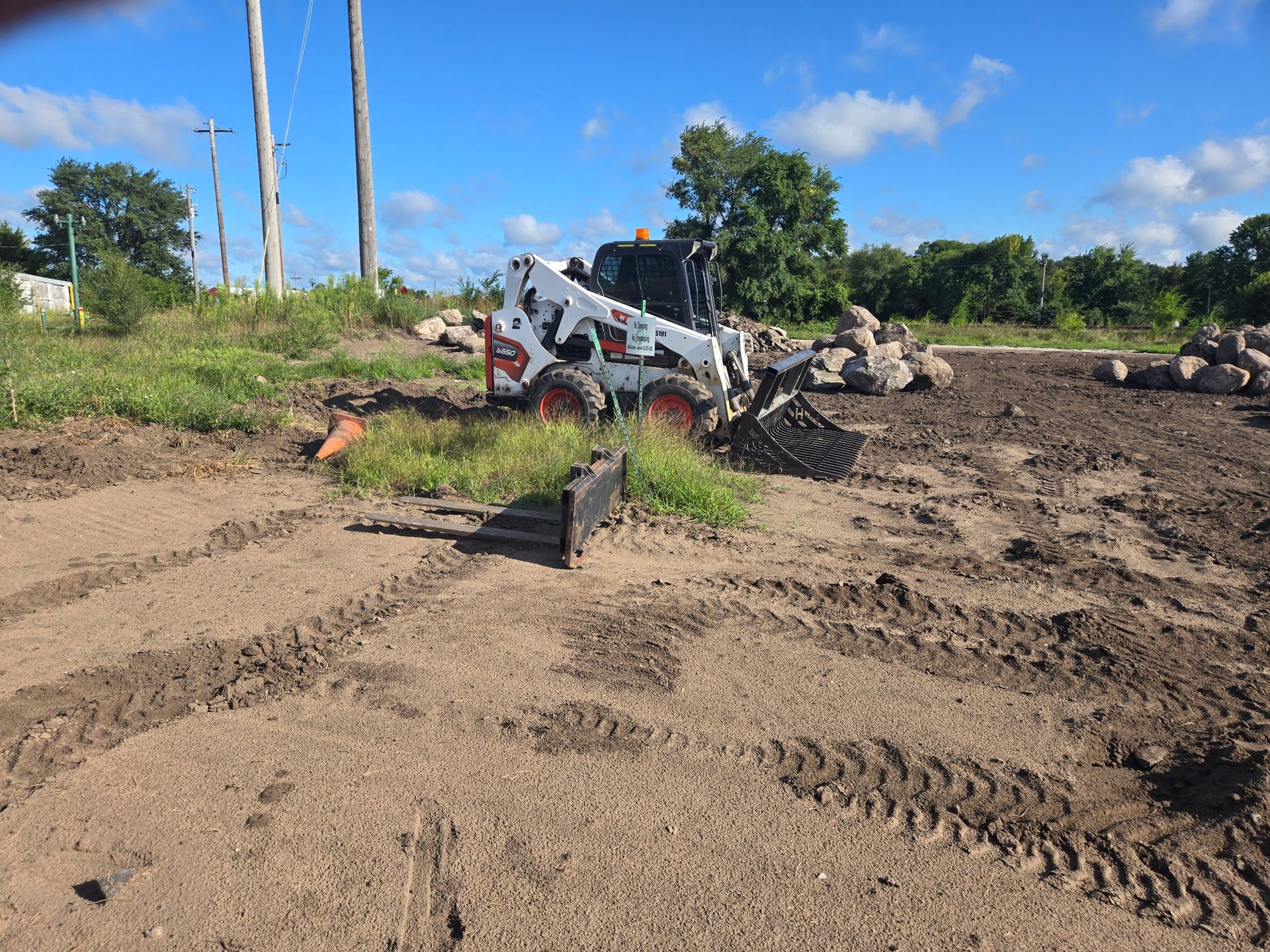Skid steer leveling muddy ground at a construction site under a blue sky