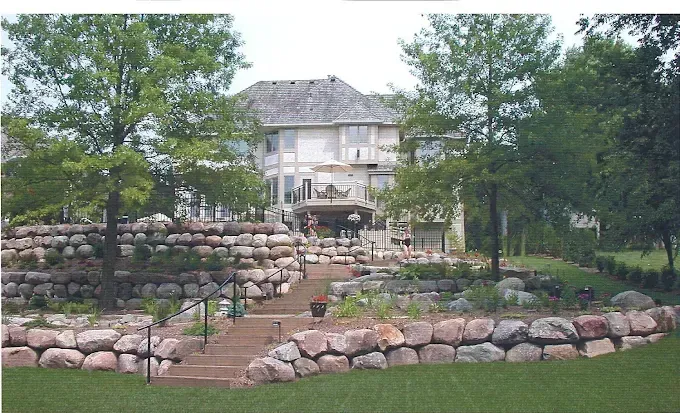 Stone house atop a terraced rock garden with trees and a lawn in front