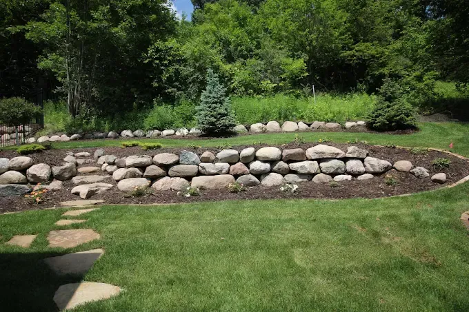 Stone retaining wall with rocks and a small evergreen tree in a green landscaped garden
