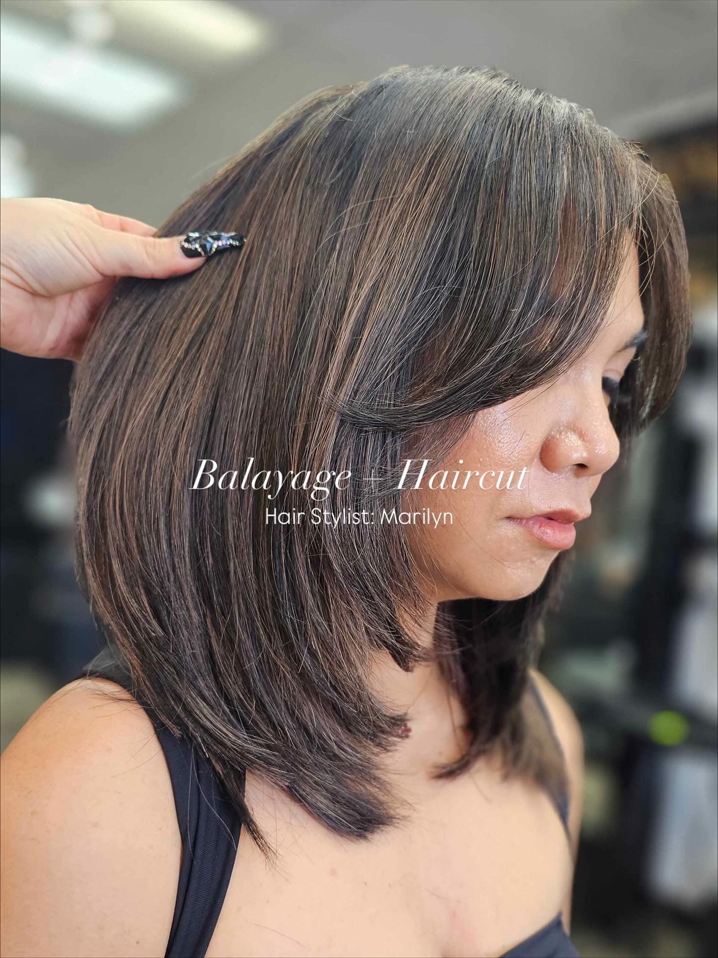 Woman with layered brown hair, side-swept bangs, at a salon. A hand touches her hair.