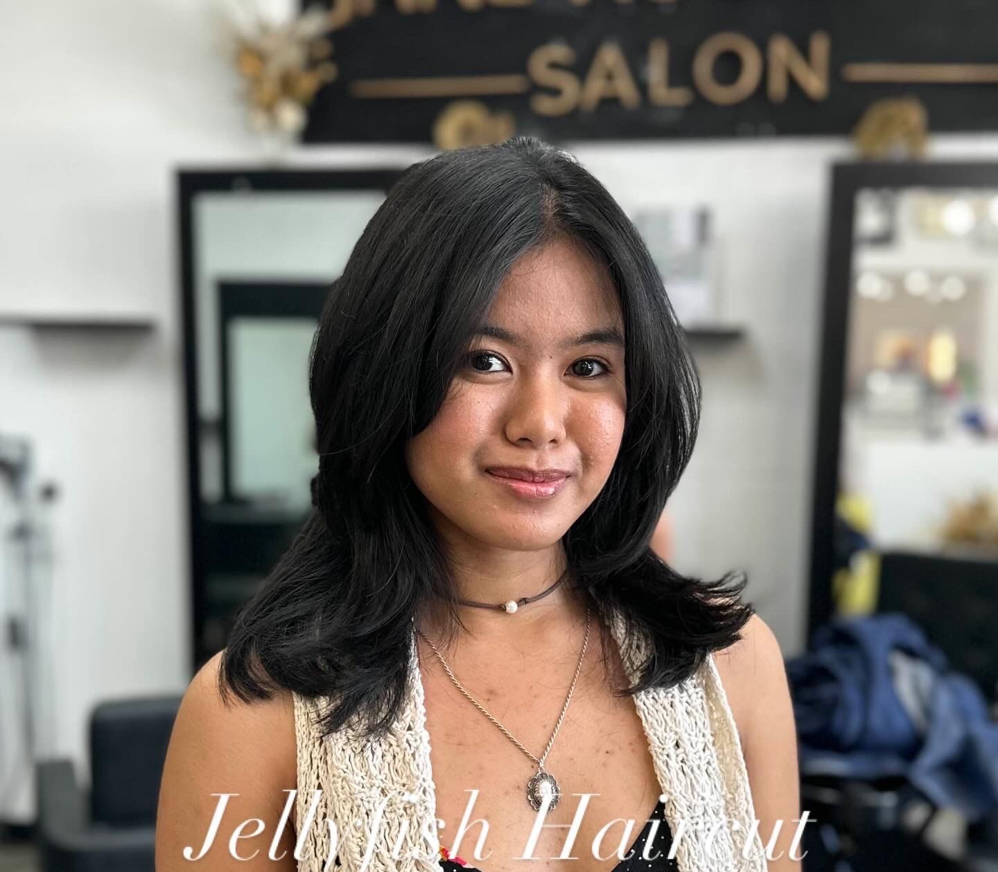Woman with black layered hair, posing at a hair salon.