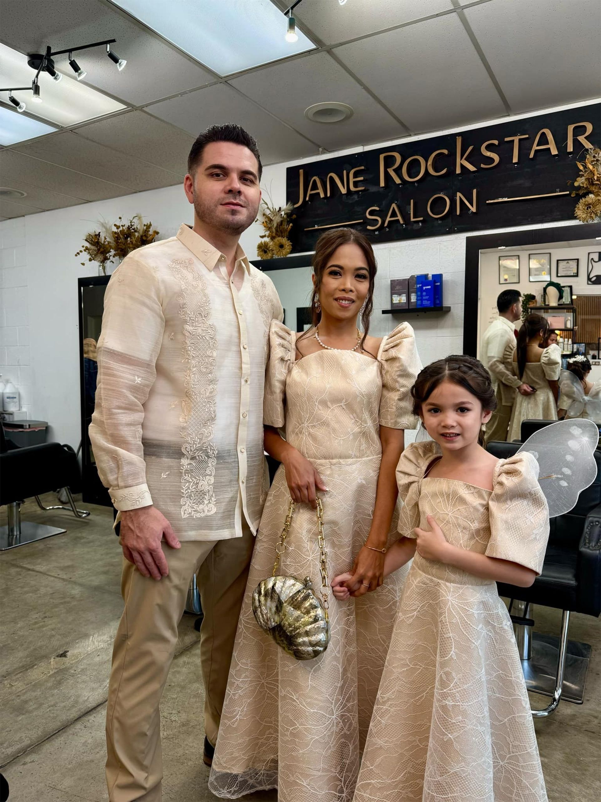 Family poses in a salon. The adults and child wear matching formal gold outfits.