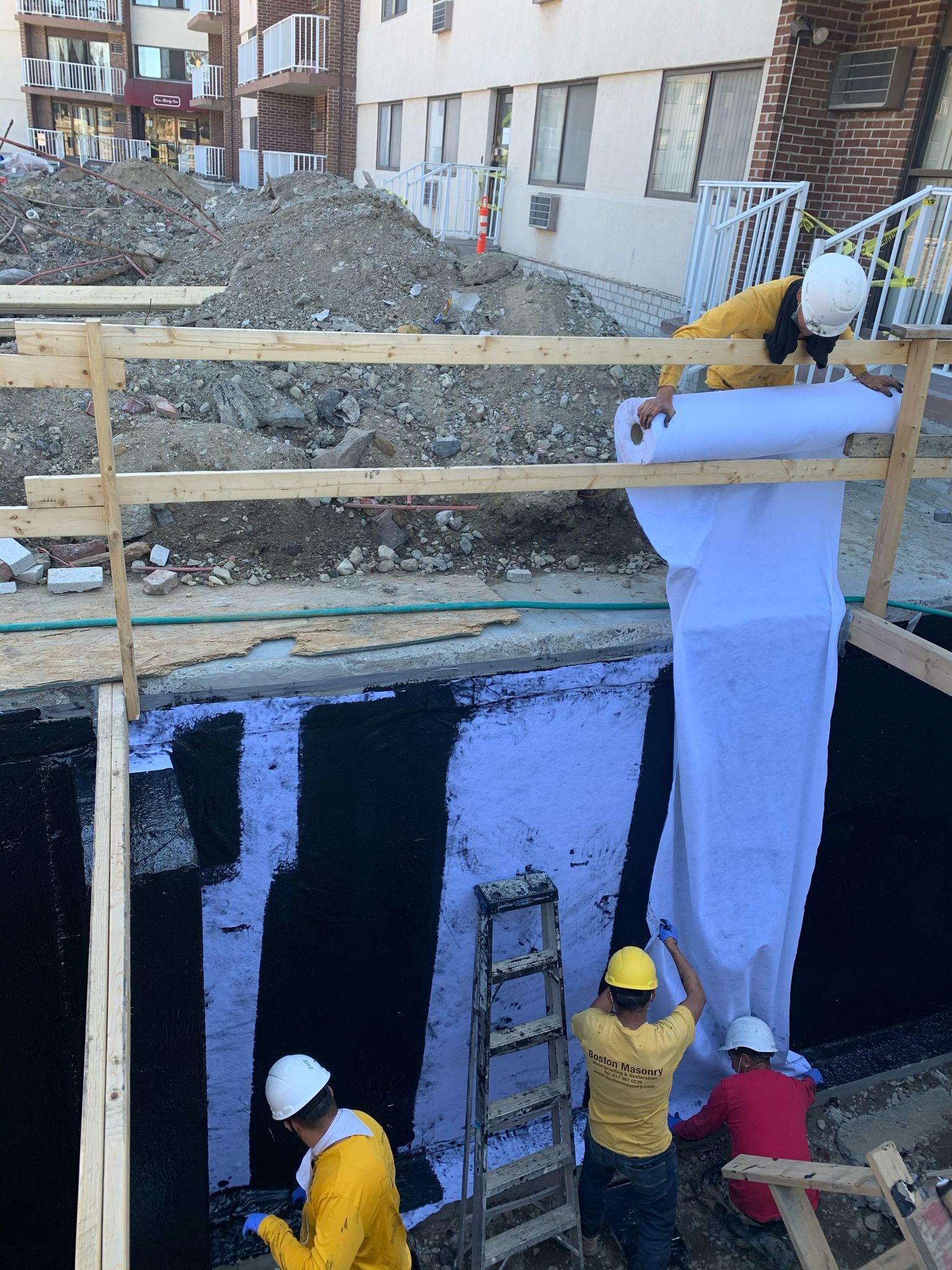 Workers are waterproofing the side of a building