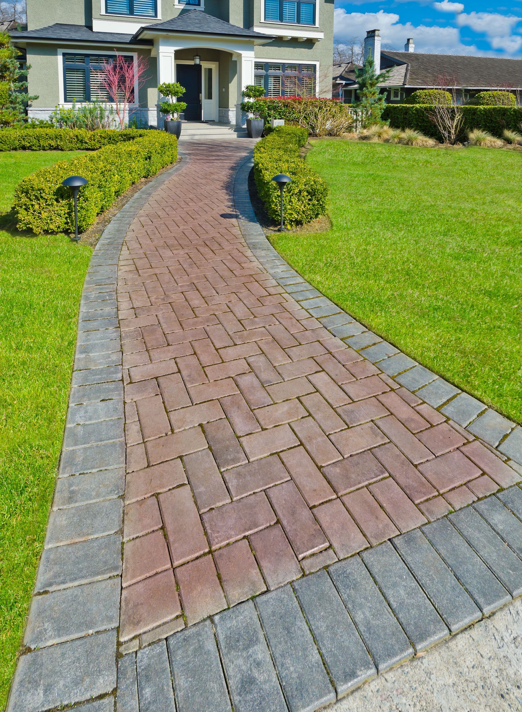 A brick walkway leading to a house with a lush green lawn