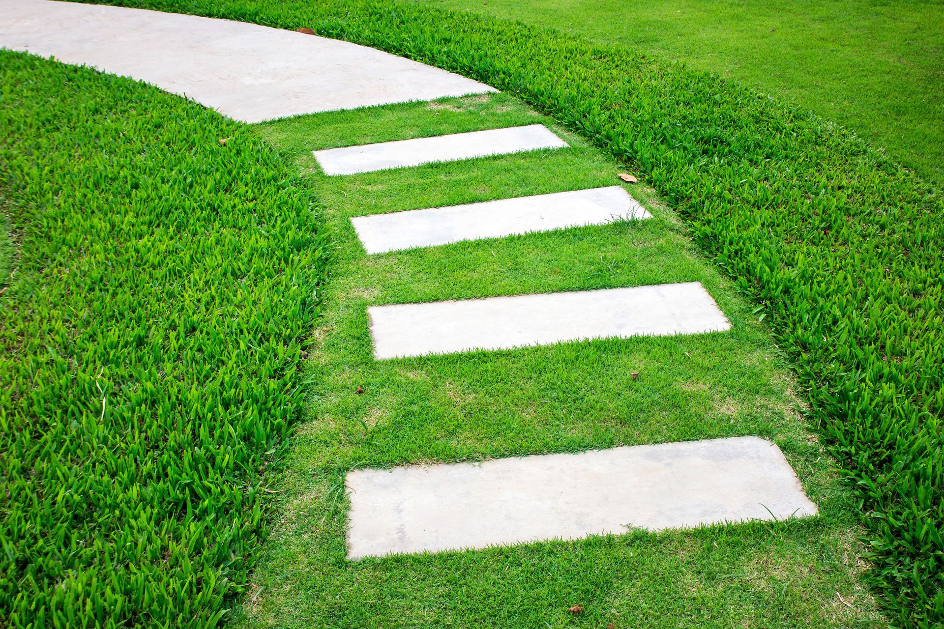 A concrete walkway going through a lush green field.