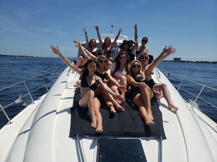 a group of women are sitting on the back of a boat with their arms in the air
