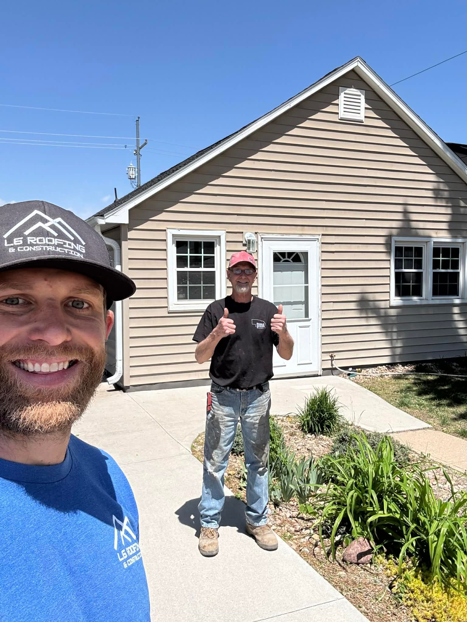 Two smiling men standing outside a beige house on a sunny day