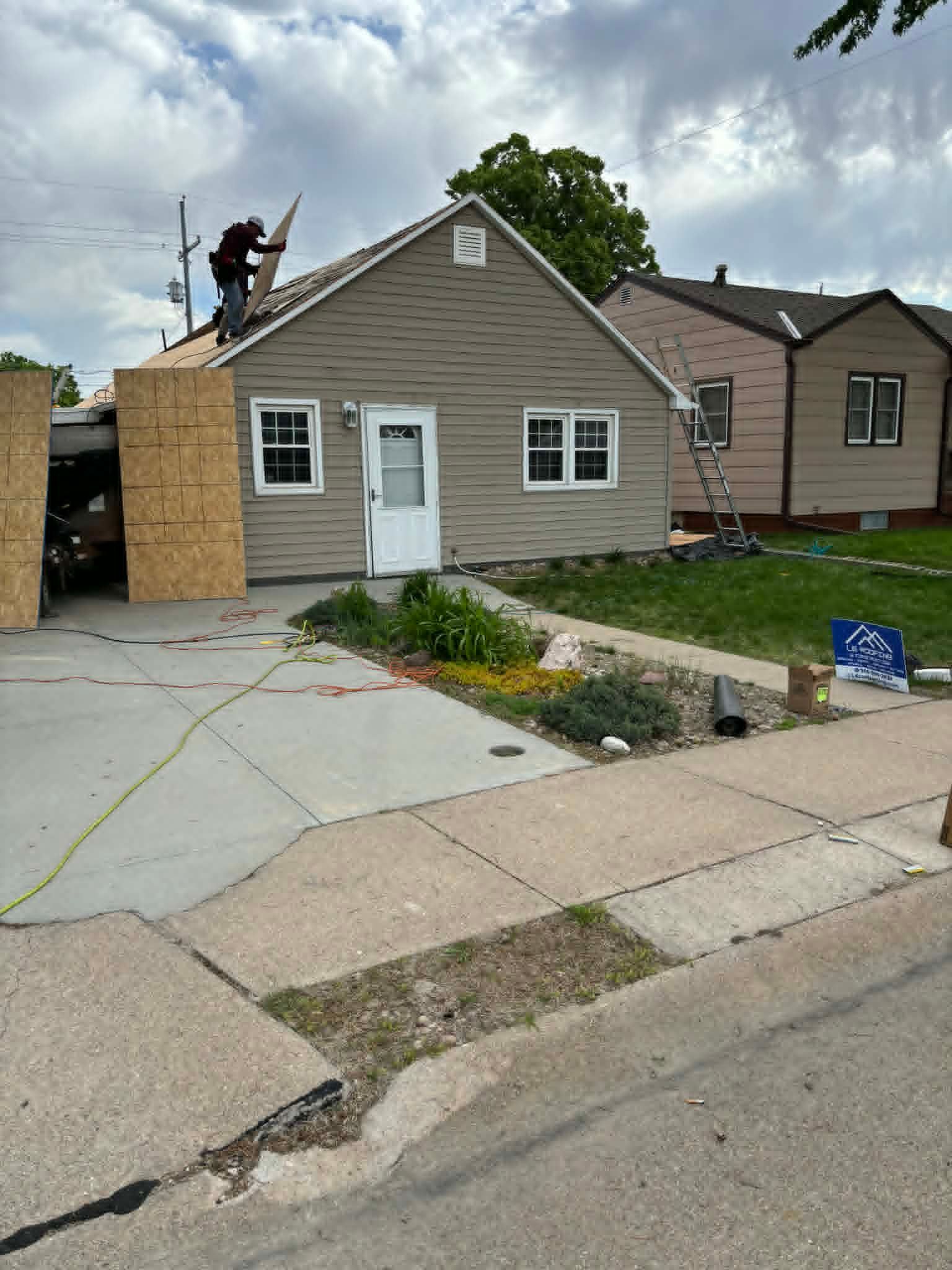 Single-story house with damaged siding, boarded window, and cracked driveway after storm damage
