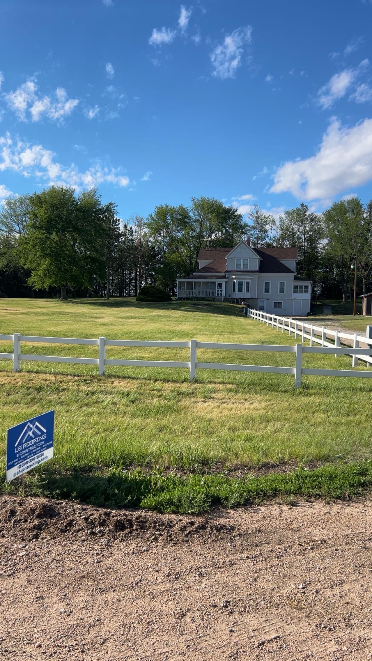 White house beyond a fenced grassy field under a blue sky with clouds