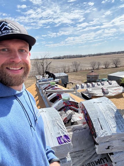 Man smiling in blue shirt beside stacked bags outdoors under a bright sky