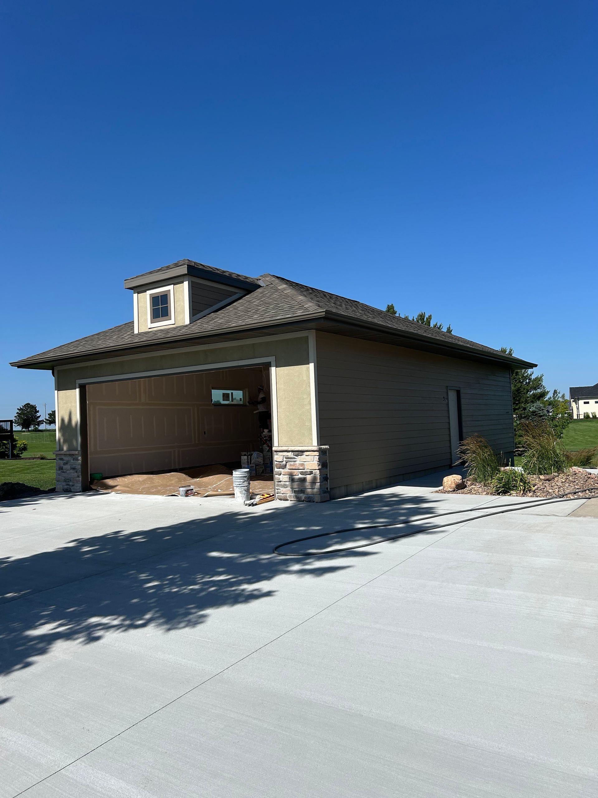 Single-story suburban house with a tiled roof, garage doors, and a driveway under a clear blue sky