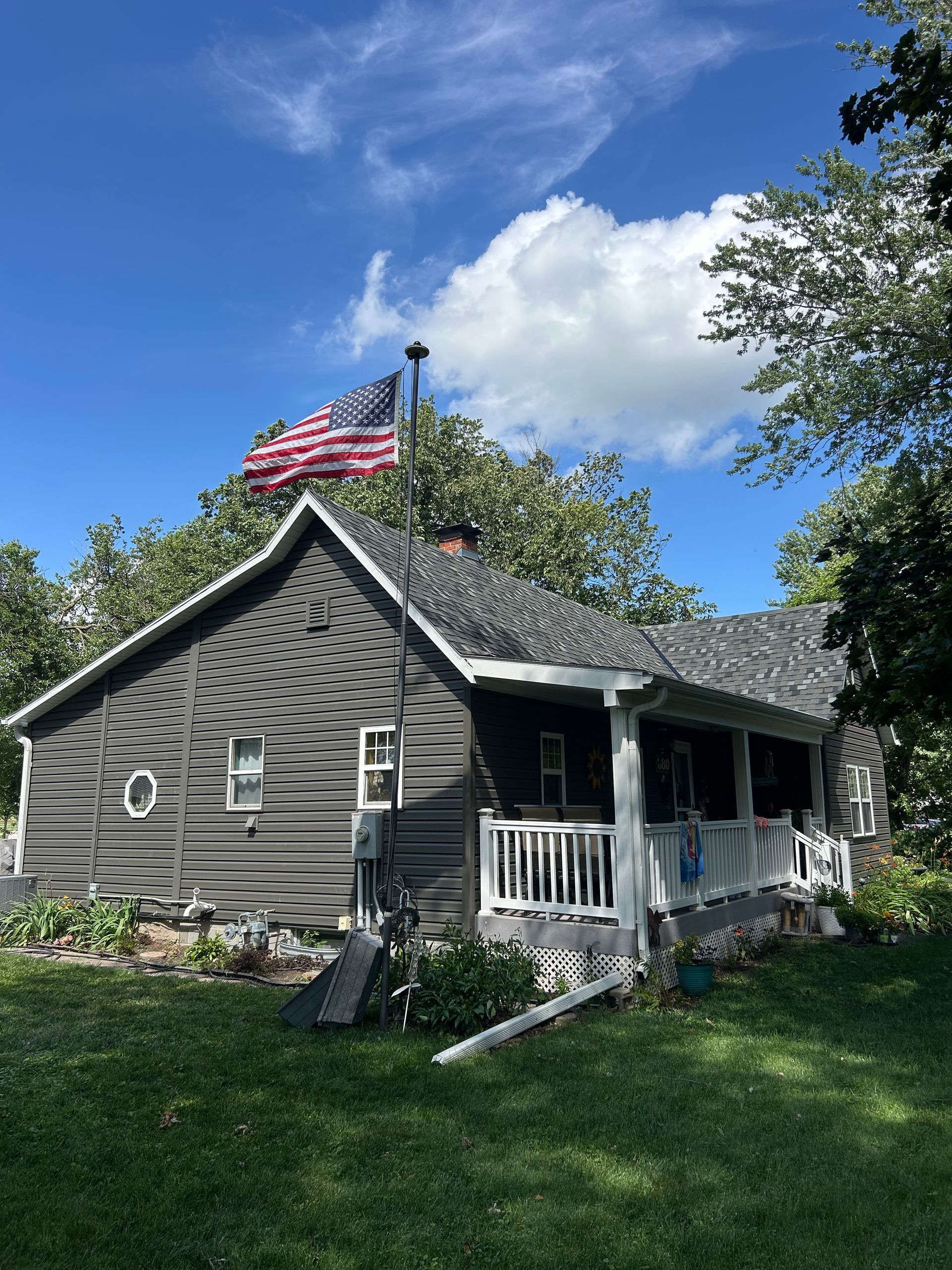 Gray cottage with white trim and porch under a blue sky, with an American flag flying above.