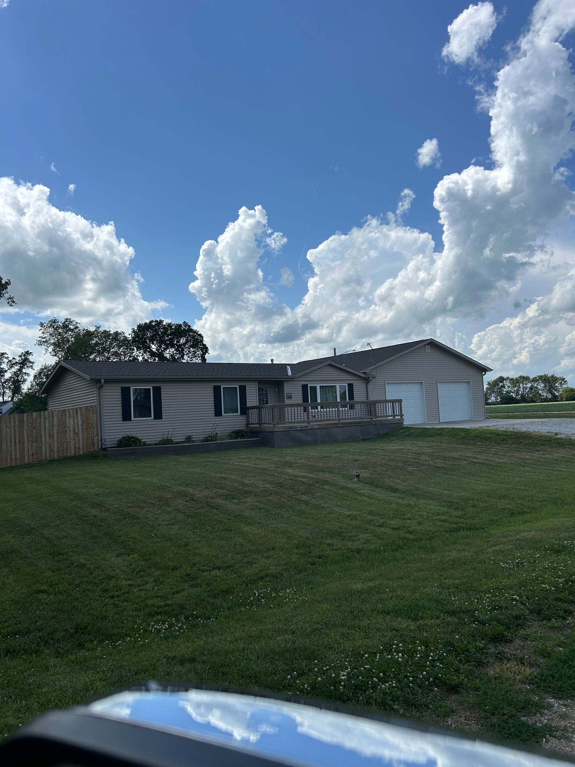 Single-story house with damaged front wall, on a grassy hill under a blue sky with clouds.