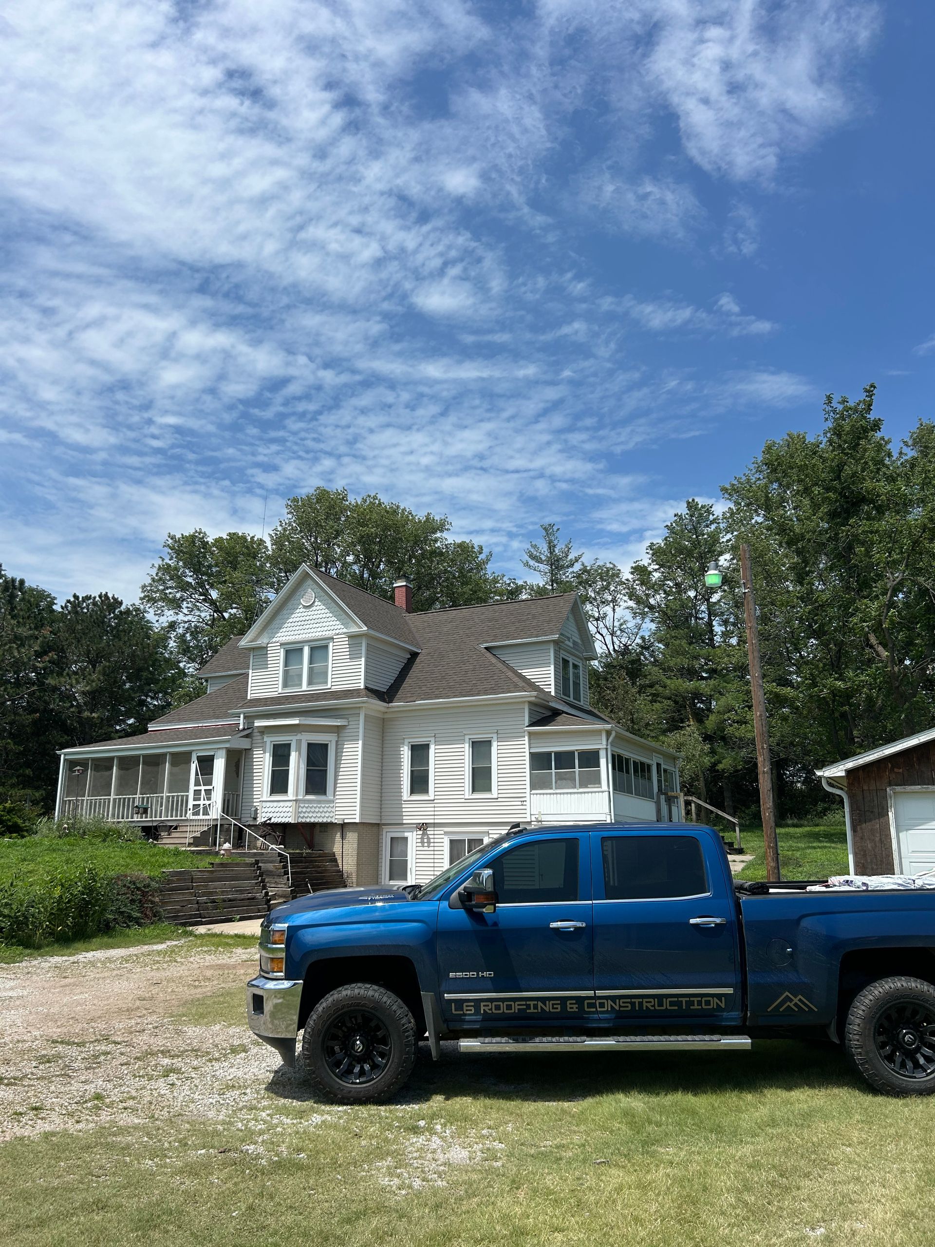 Blue pickup truck parked in front of a white house under a partly cloudy sky.