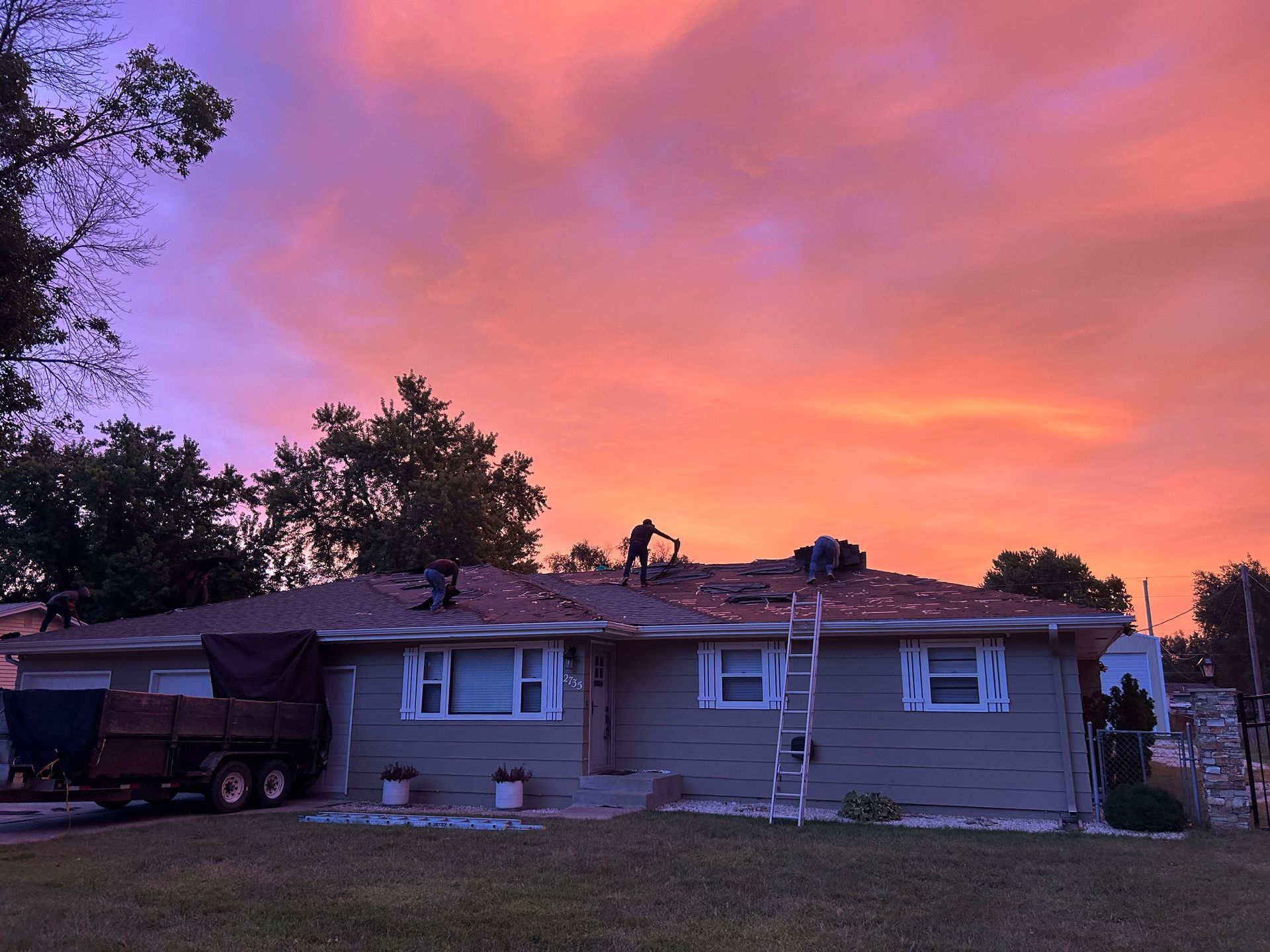 Single-story house at sunset under a pink-orange sky, with trees silhouetted around it.
