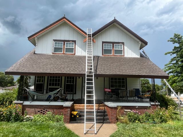 Front view of a white house with a ladder reaching the roof and a cloudy sky overhead