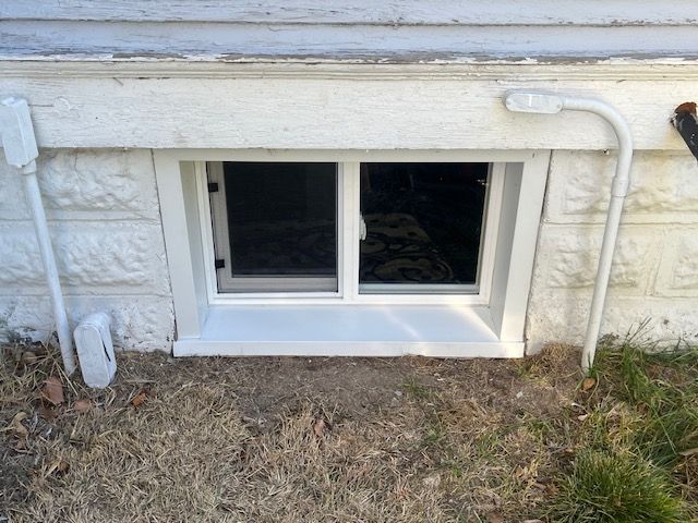 Basement window with white trim and stone foundation, with a pipe running along the wall above it.