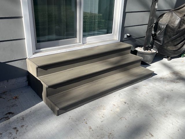Wooden three-step deck stairs leading to a sliding glass door beside a patio with a chair and potted plant
