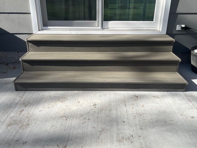 Three-step gray deck stairs leading to a sliding glass door on a concrete patio
