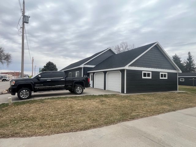 Black pickup truck parked beside a gray garage with white trim on a cloudy day