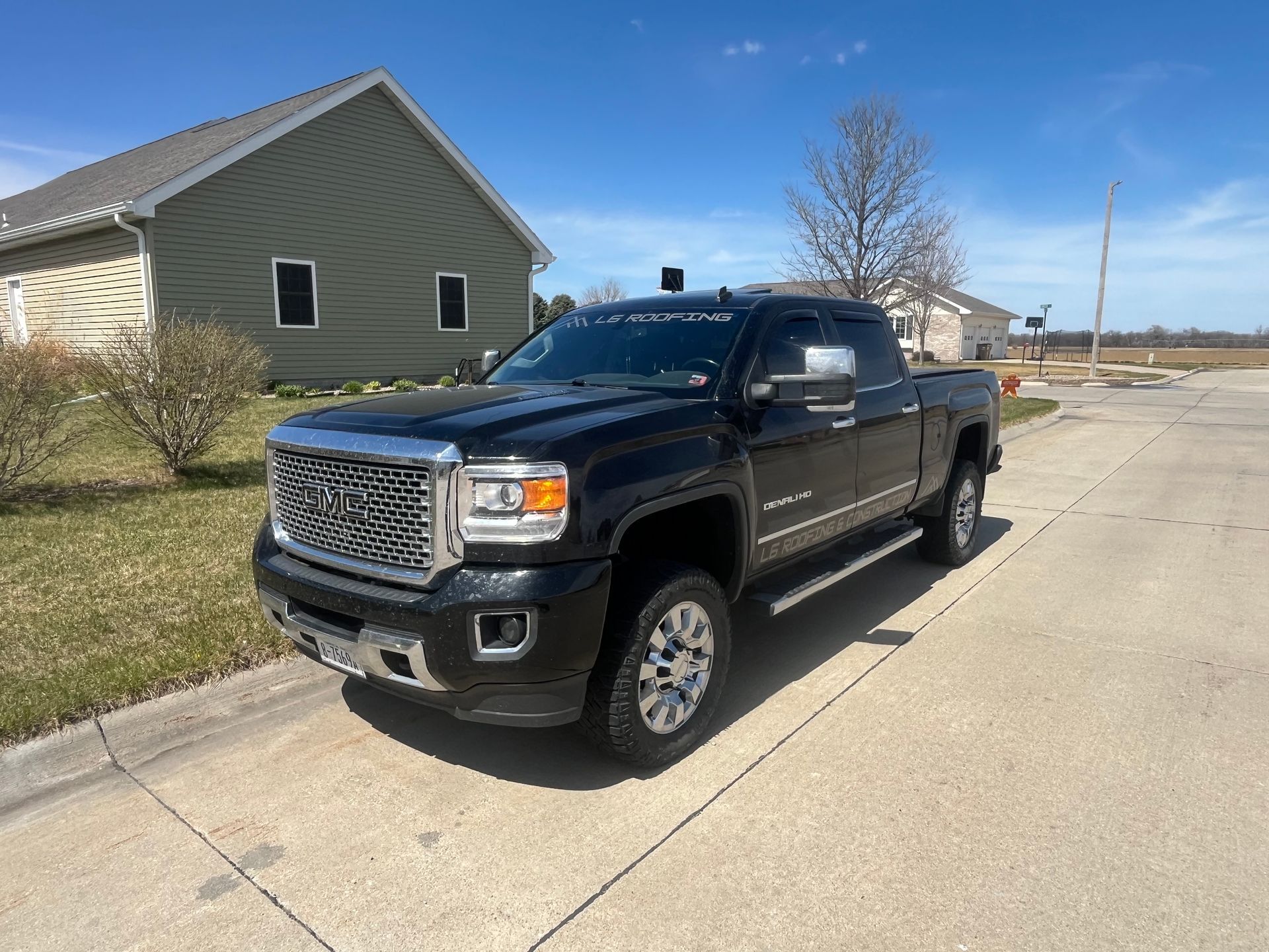 Black pickup truck parked on a suburban street beside a house on a sunny day